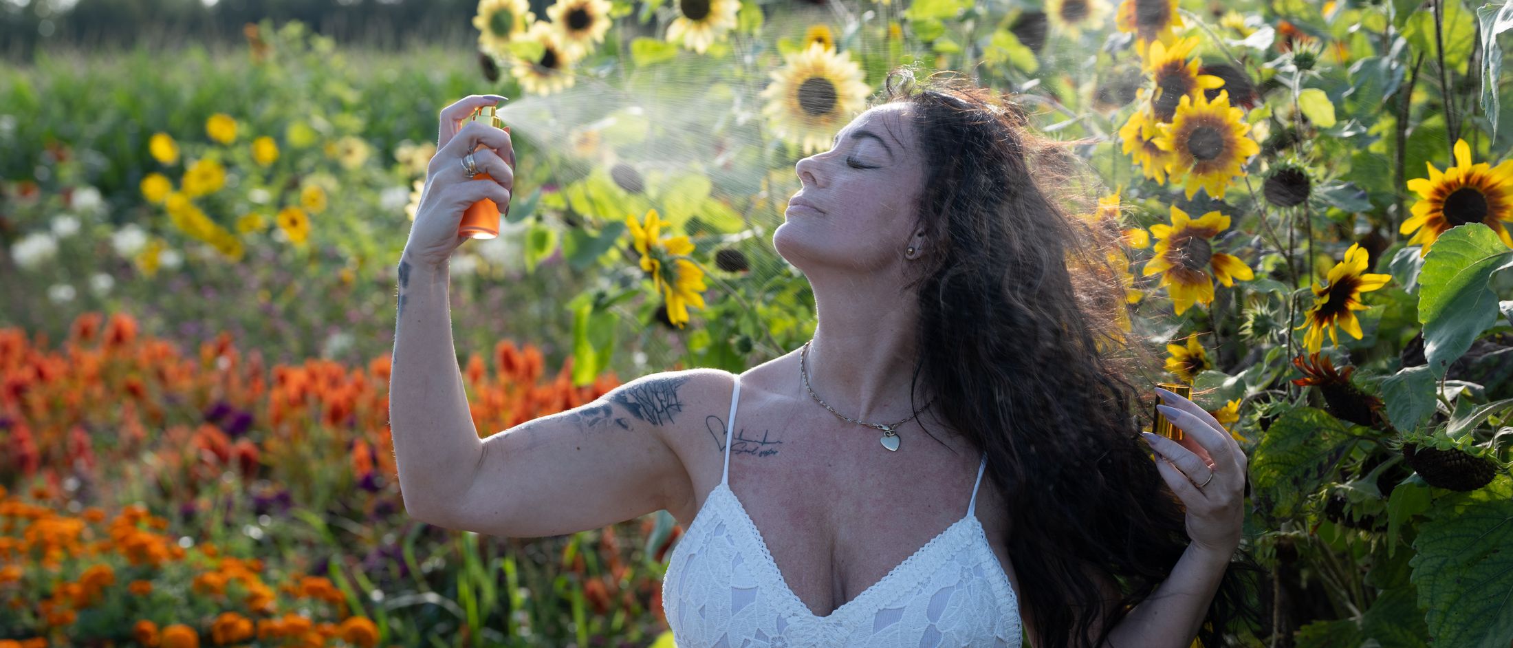 Une femme vaporise la brume tonique Lotus Solaire de B&F Essence dans un champ de tournesols